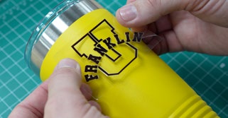Crisp transparent logo sticker with black lettering being applied to a bright-colored canteen