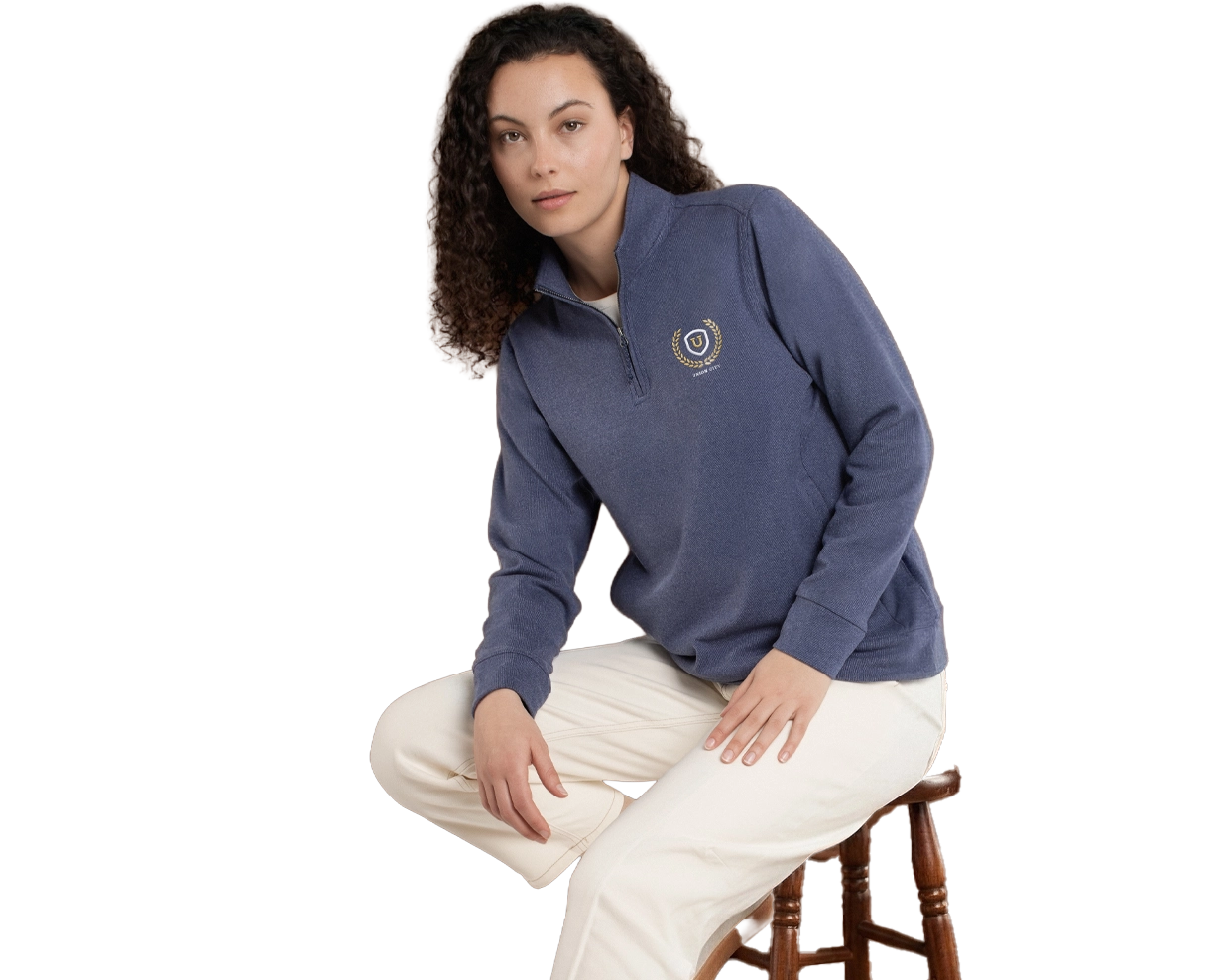 Woman wearing a blue-grey quarter-zip wool windbreaker, and some off-white pants, sitting on a stool