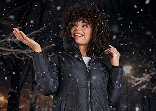 A woman in a zip-up puffer jacket holding up her hand to the falling snow
